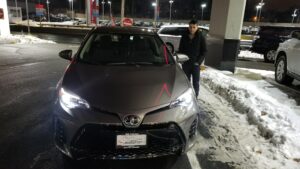 A man standing next to a parked car in the snow.