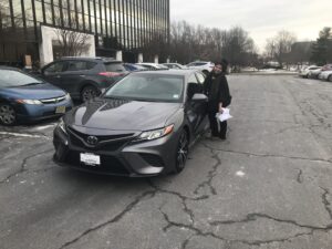 A woman is standing next to a car in the parking lot.