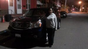 A woman standing next to a black car on the street.